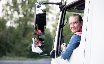
Lkw-Fahrerin blickt lächelnd aus dem geöffneten Seitenfenster ihres Fahrzeugs