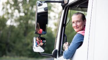 
Lkw-Fahrerin blickt lächelnd aus dem geöffneten Seitenfenster ihres Fahrzeugs
