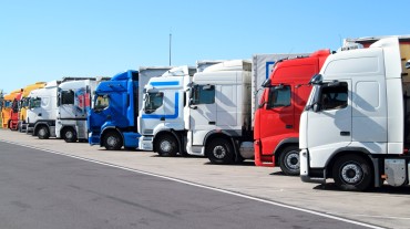
Reihe geparkter Lkw in verschiedenen Farben auf einem Parkplatz bei blauem Himmel