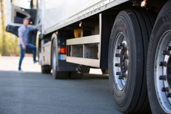 
Nahaufnahme von Lkw-Reifen auf einem Parkplatz, im Hintergrund steigt ein Fahrer in das Fahrzeug ein.