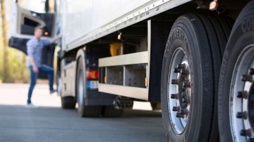 
Nahaufnahme von Lkw-Reifen auf einem Parkplatz, im Hintergrund steigt ein Fahrer in das Fahrzeug ein.