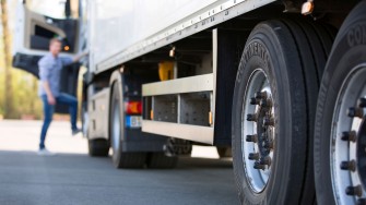 
Nahaufnahme von Lkw-Reifen auf einem Parkplatz, im Hintergrund steigt ein Fahrer in das Fahrzeug ein.