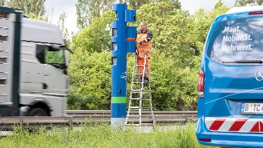 
Außendienstmitarbeiter wartet eine Kontrollsäule an einer Straße, während ein Lkw vorbeifährt