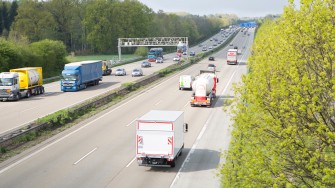
Lkw und Pkw fahren auf einer Autobahn, auf der eine Kontrollbrücke auf einer Seite der Fahrbahn steht.