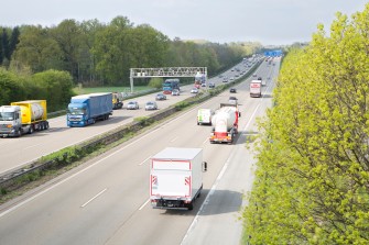
Lkw und Pkw fahren auf einer Autobahn, auf der eine Kontrollbrücke auf einer Seite der Fahrbahn steht.