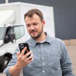 
Mann blickt auf ein Smartphone, während im Hintergrund ein Lkw steht