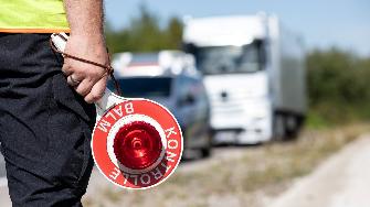 
Mitarbeiter des Bundesamts für Logistik und Mobilität hält eine Kontrollkelle; im Hintergrund stehen ein Kontrollfahrzeug und ein Lkw am Straßenrand