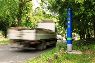 
Ein Lkw fährt auf einer von Bäumen gesäumten Straße an einer Kontrollsäule vorbei