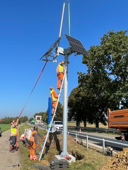 
Mehrere Personen installieren einen Mast mit Solarmodulen an einer Kontrollsäule.