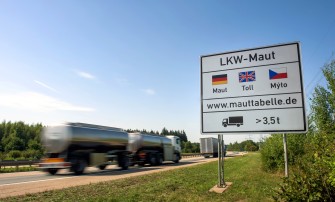
Hinweisschild zur Lkw-Maut mit vorbeifahrendem Lkw auf einer Autobahn