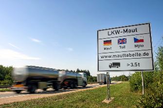 
Hinweisschild zur Lkw-Maut mit vorbeifahrendem Lkw auf einer Autobahn
