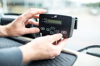 
Zwei Hände halten eine On-Board Unit zur Erfassung der Lkw-Maut im Fahrerhaus eines Lkw
