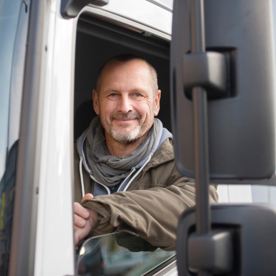 
Lächelnder Fahrer blickt aus dem geöffneten Seitenfenster seines Lkw