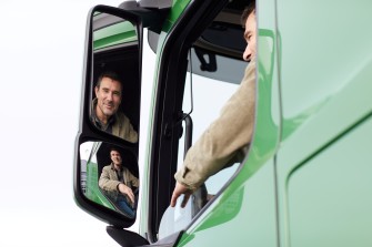 
Lkw-Fahrer schaut aus dem Fenster seines Lastwagens und spiegelt sich im Seitenspiegel.