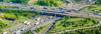
Luftaufnahme eines stark befahrenen Autobahnkreuzes mit mehreren Fahrbahnen und Lkw sowie Pkw.