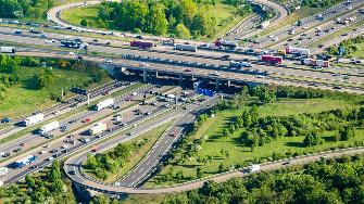 
Luftaufnahme eines stark befahrenen Autobahnkreuzes mit mehreren Fahrbahnen und Lkw sowie Pkw.