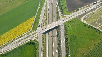 
Luftaufnahme einer Straßenbrücke, die über eine andere Straße verläuft, umgeben von Feldern.