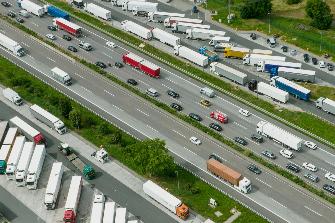 
Luftaufnahme einer Autobahn mit Stau und geparkten Lkw neben grüner Landschaft.