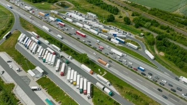 
Luftaufnahme einer Autobahn mit Stau und geparkten Lkw neben grüner Landschaft.
