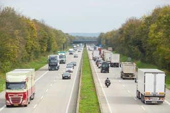 
Stark befahrene Autobahn mit Lkw und Pkw, umgeben von Bäumen