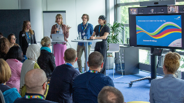 
Vortragende sprechen beim Diversity-Tag vor Publikum, daneben eine Präsentation auf einem Bildschirm