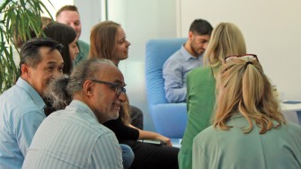 
Personengruppe in Büroumgebung bei Gesprächsrunde vor moderner Einrichtung.