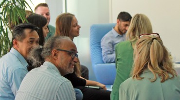 
Personengruppe in Büroumgebung bei Gesprächsrunde vor moderner Einrichtung.