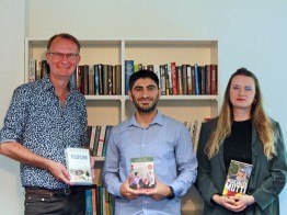 
Andreas Kossert, Fahed Khalili und Elina Penner stehen vor Bücherregal und halten Bücher in den Händen.