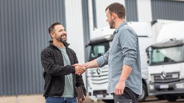 
Zwei Männer geben sich vor mehreren Lkw die Hand