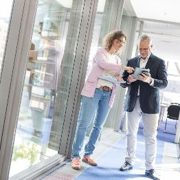 
Zwei Mitarbeitende von Toll Collect stehen in einem Gang und blicken auf ein Tablet