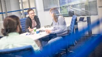 
Drei Personen sitzen in einem Besprechungsraum an einem Tisch und unterhalten sich miteinander.