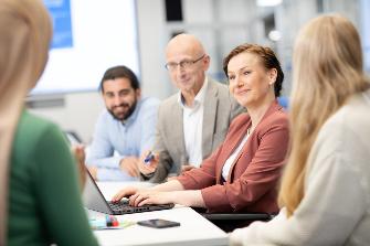 
Mehrere Personen sitzen an einem Tisch in einem Besprechungsraum und tauschen sich miteinander aus.