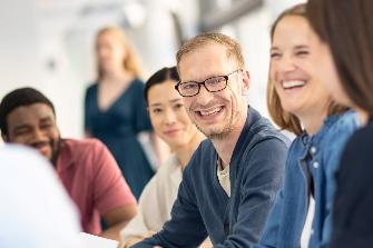 
Mehrere Personen sitzen zusammen und lächeln sich in einer Besprechung an.