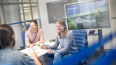 
Mitarbeitende sitzen lächelnd in einem Besprechungsraum an einem Tisch