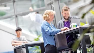 
Zwei Personen arbeiten gemeinsam an einem Laptop an einem Stehtisch in einem modernen Büro