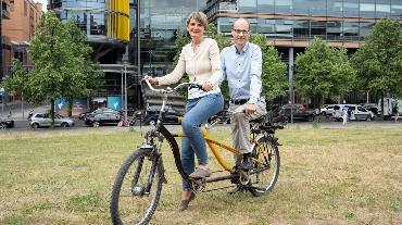 
Portrait einer Mitarbeiterin und eines Mitarbeiters gemeinsam auf Tandem