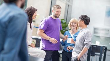 
Mehrere Personen stehen in einem Büro zusammen, lachen und unterhalten sich in einer Pause.