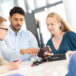 
Drei Personen sitzen an einem Tisch und betrachten gemeinsam eine On-Board-Unit
