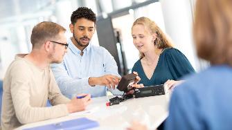 
Drei Personen sitzen an einem Tisch und betrachten gemeinsam eine On-Board-Unit