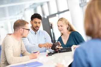 
Drei Personen sitzen an einem Tisch und betrachten gemeinsam eine On-Board-Unit