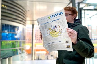 
Person liest eine Zeitung in einem modernen Gebäudeeingang mit Glasfassade.