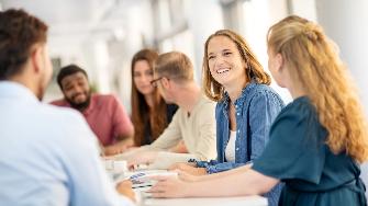 
Mehrere Personen sitzen an einem Tisch in einem Büro und unterhalten sich lächelnd miteinander.
